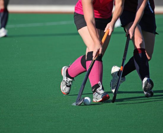 Two women players contest for the ball in a game of field hockey
